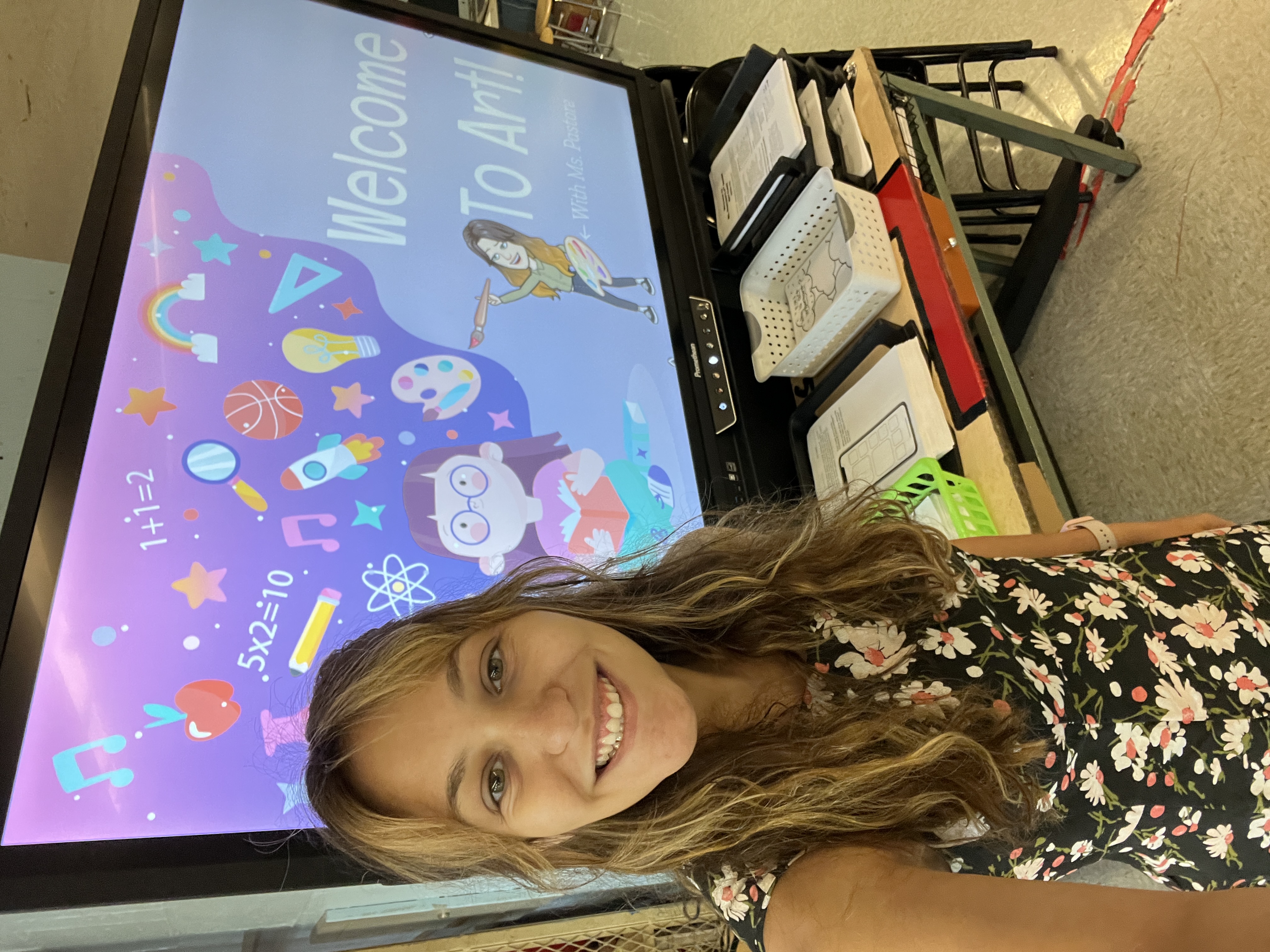 smiling young woman in an art classroom in front of a large screen