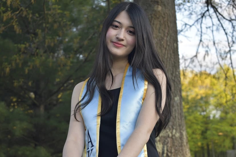 young woman with graduation sash standing in front of a tree