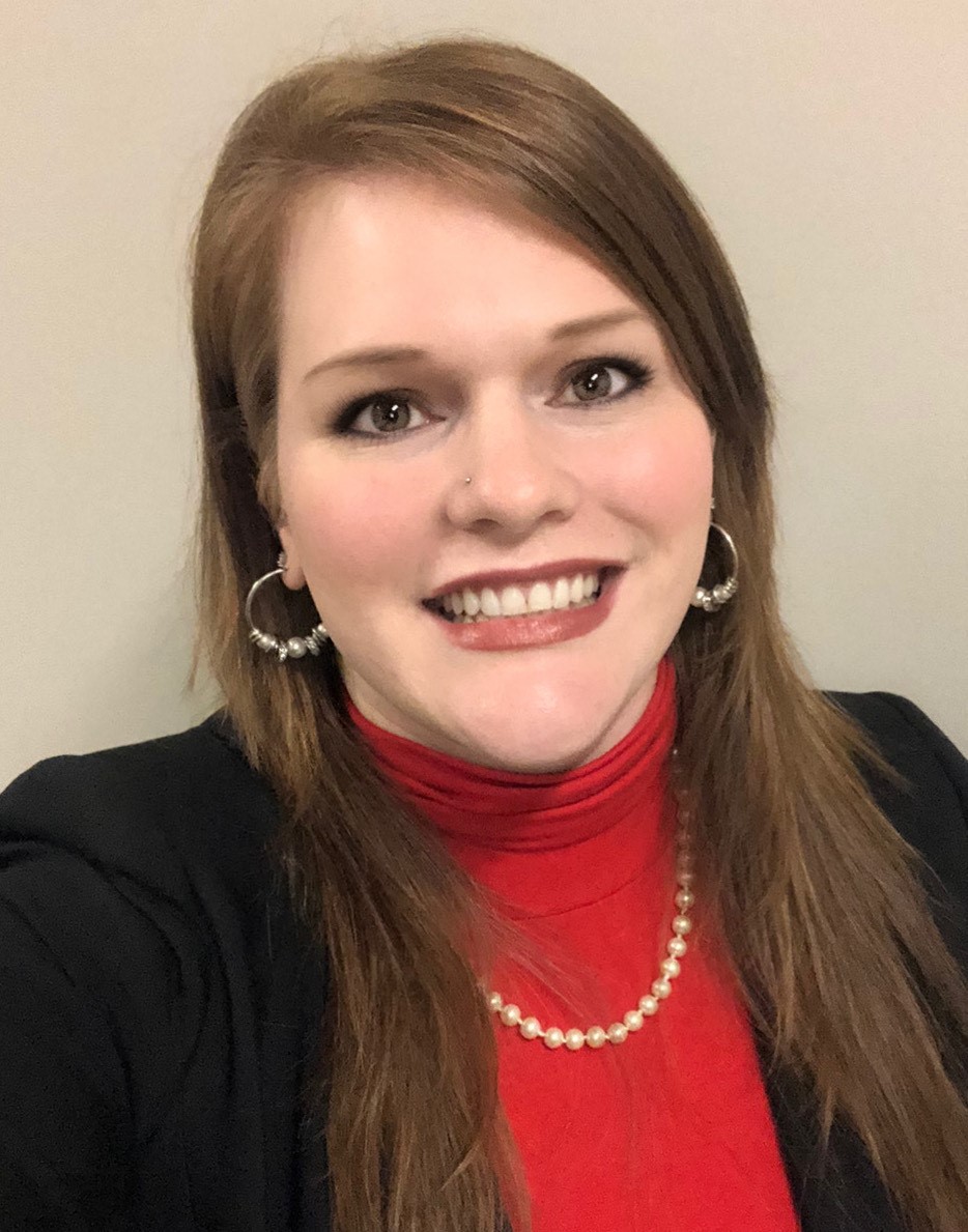 smiling young woman with long red hair and red turtleneck with black jacket wearing a pearl necklace