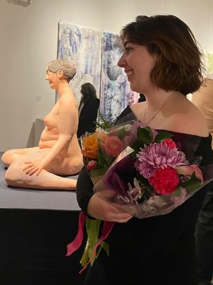 a student holding roses in front of their ceramic work at a Bachelor's of Fine Arts Thesis Exhibition at SUNY New Paltz