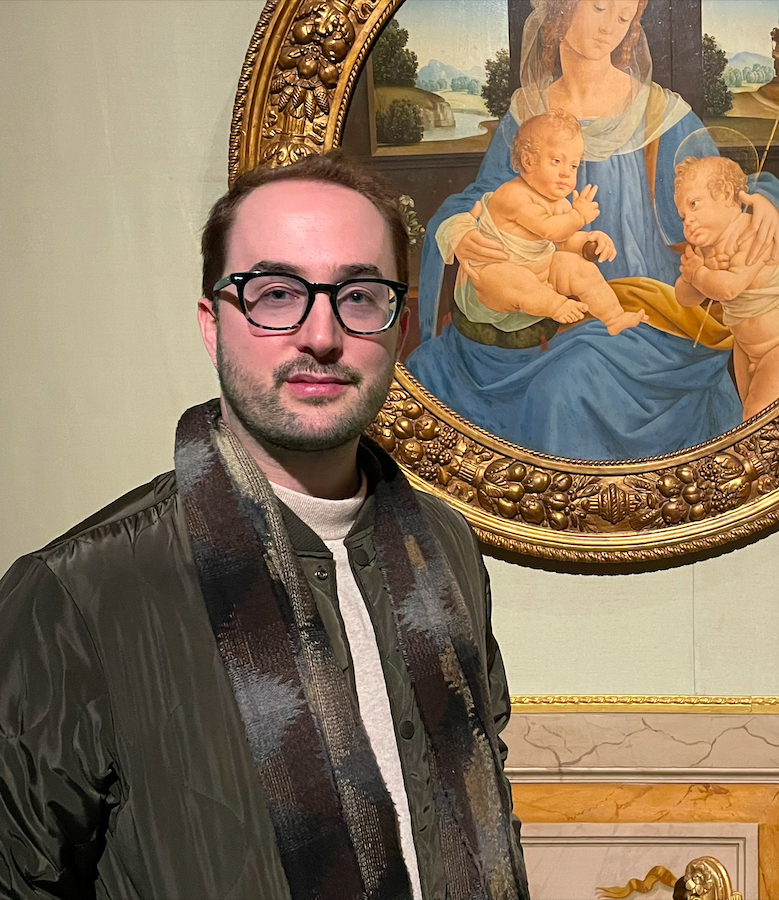 person with short brown hair, glasses and jacket in front of Botticelli painting