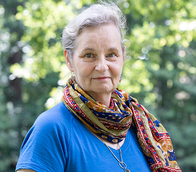 person with gray hair, blue sweater and multi-colored scarf, smiling