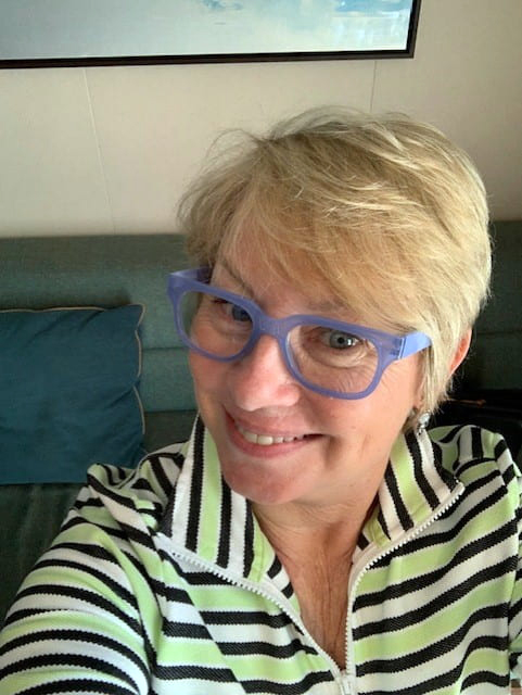 person with short blond hair and blue eyeglasses smiling