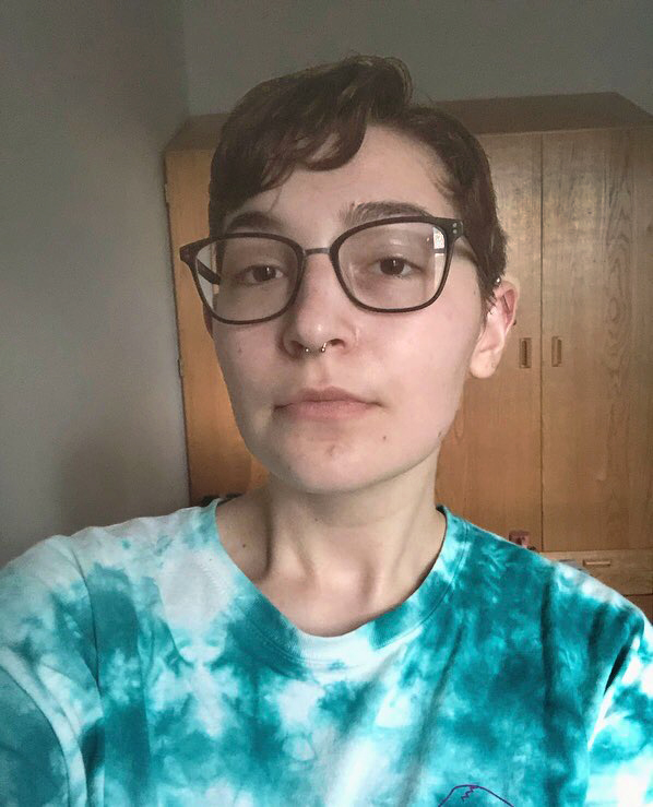 person with short brown hair and glasses wearing a tie-dye shirt