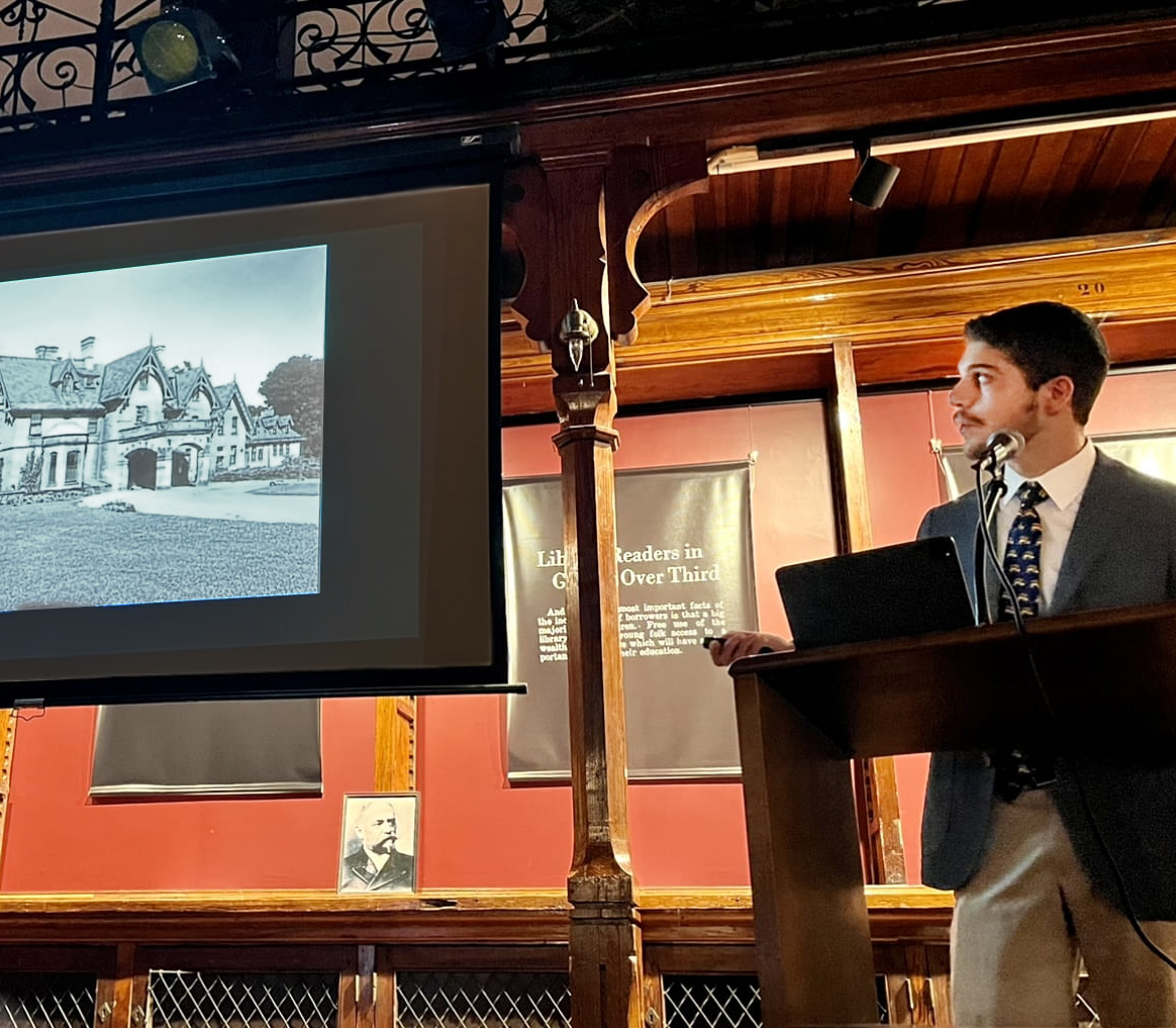 person with a beard wearing a jacket and tie delivering a lecture on architecture