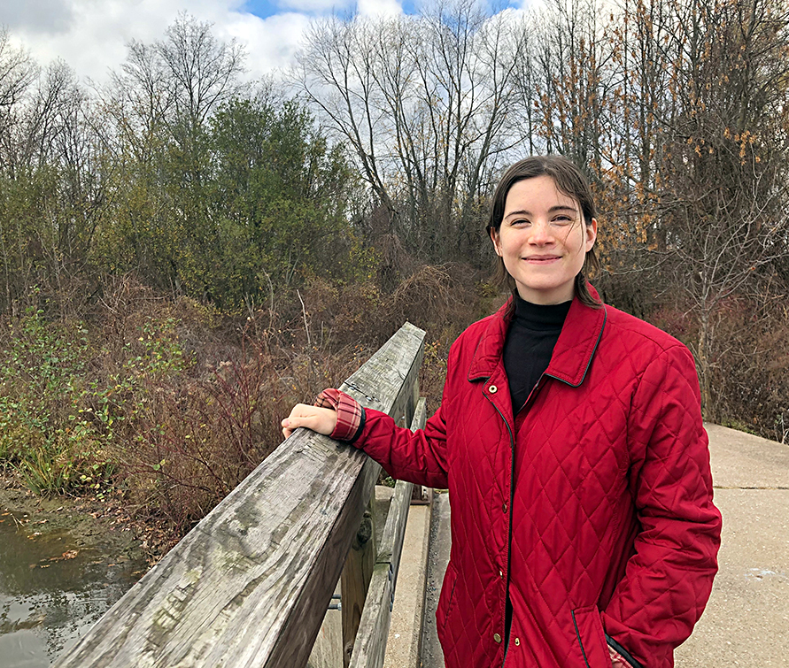 person standing on a bridge with a red coat, smiling