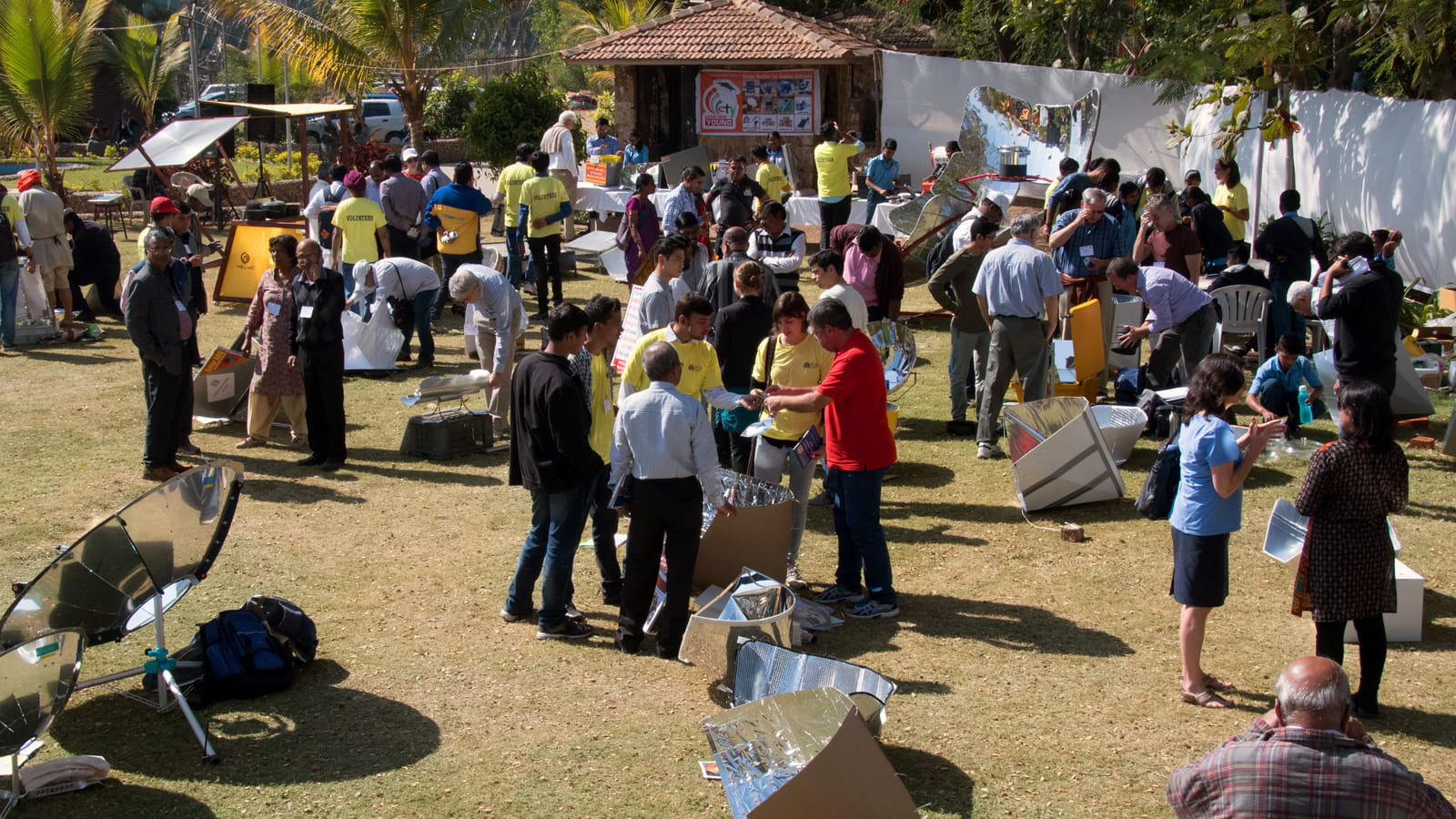 people gathered outside in small groups discussing solar cookers