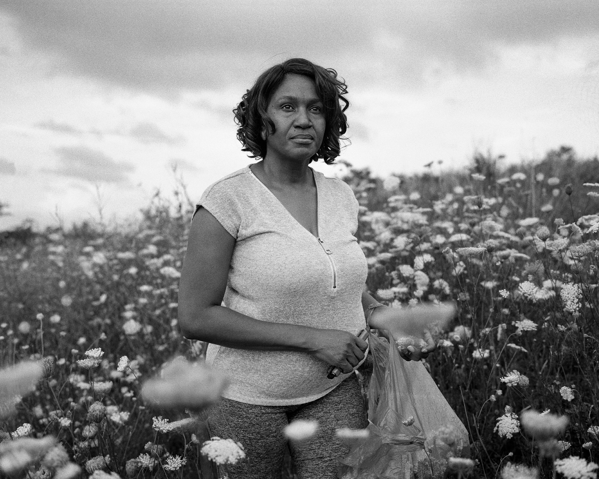 black and white photo of woman picking wildflowers, looking at camera