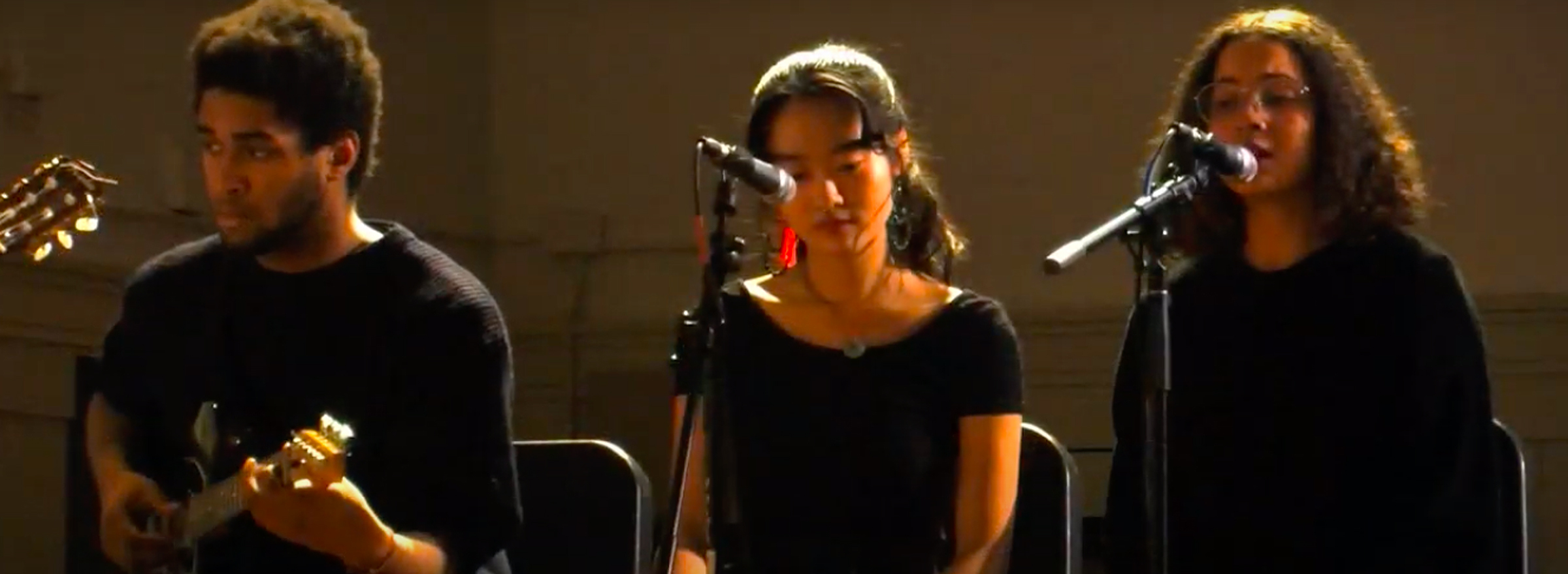 3 students playing guitar and singing in front of microphones